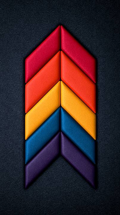 A vertical upward-pointing chevron formed by soft padded fabric segments in red, orange, yellow, blue, and purple against a dark textured background.
